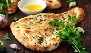 Indian naan bread with garlic butter on wooden table.
